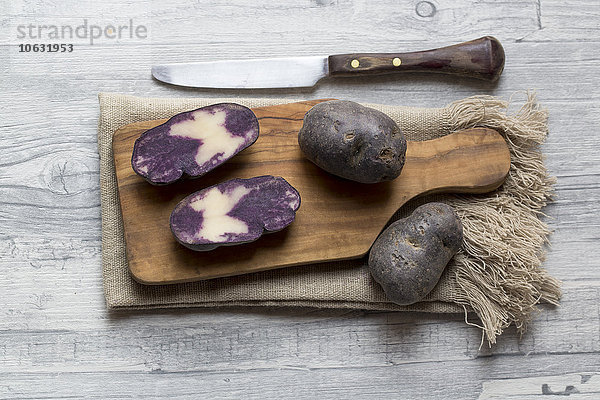 Geschnittene und ganze violette Kartoffeln auf Holzbrett und Tuch
