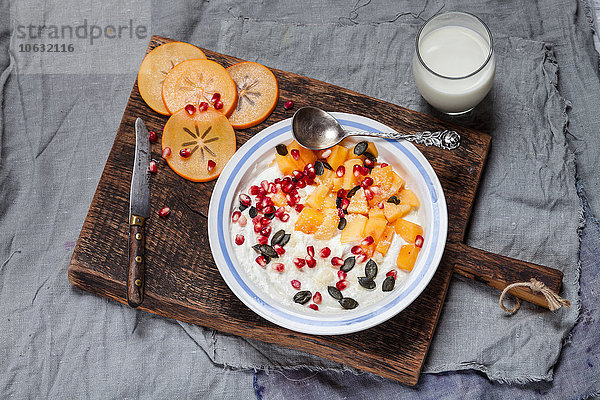 Schale aus Naturjoghurt  Kaki  Granatapfelsamen  Mandel- und Kürbiskernen