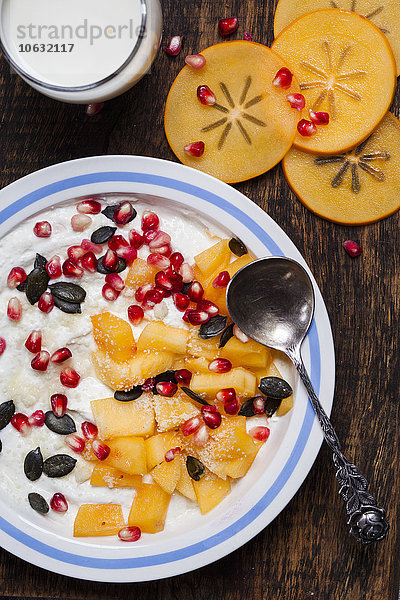 Schale aus Naturjoghurt  Kaki  Granatapfelsamen  Mandel- und Kürbiskernen