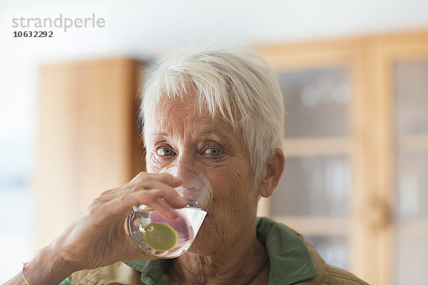 Porträt einer weißhaarigen Seniorin  die ein Glas Wasser trinkt.