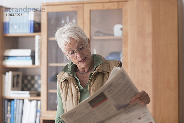 Porträt der weißhaarigen Seniorin beim Zeitungslesen zu Hause