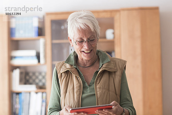 Porträt einer weißhaarigen Seniorin beim Betrachten ihres digitalen Tabletts zu Hause