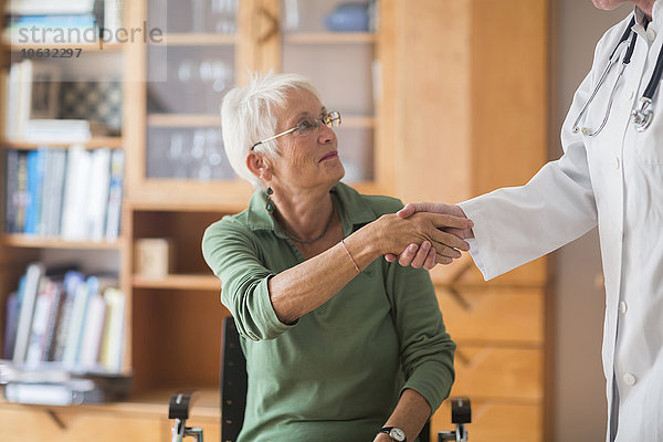 Weißhaarige Seniorin beim Händeschütteln mit ihrem Arzt