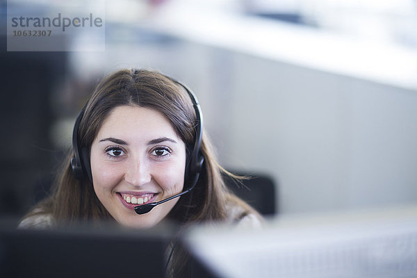 Porträt einer lächelnden jungen Frau mit Kopfhörer am Arbeitsplatz