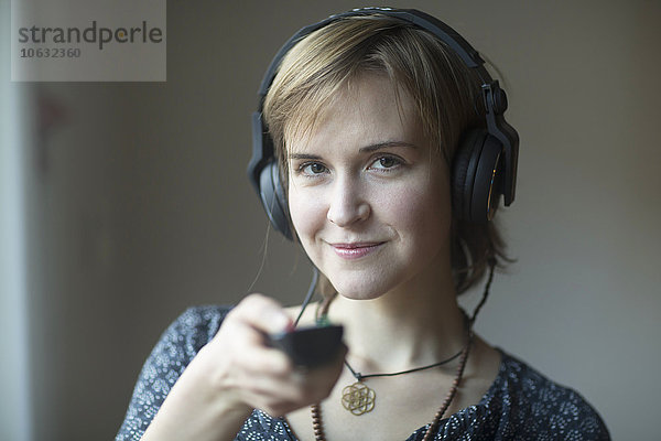 Portrait der lächelnden jungen Frau mit Kopfhörer und Fernbedienung