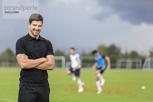 Porträt eines lächelnden Trainers mit Fußballspielern im Hintergrund