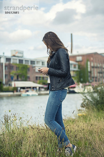 Deutschland  Münster  junge Frau auf einer Wiese am Stadthafen mit Blick auf ihr Smartphone