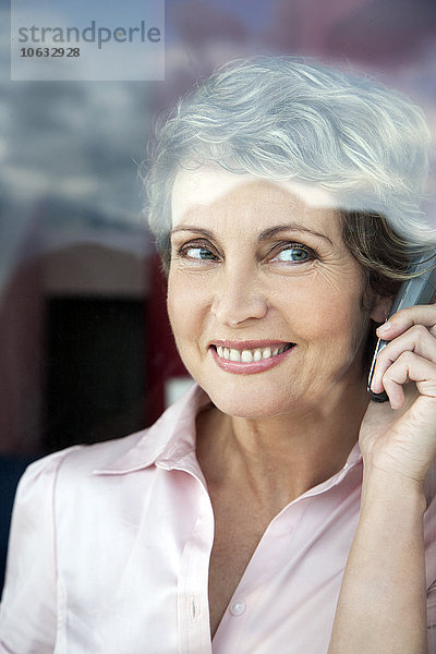 Porträt einer lächelnden Frau beim Telefonieren mit Blick durchs Fenster