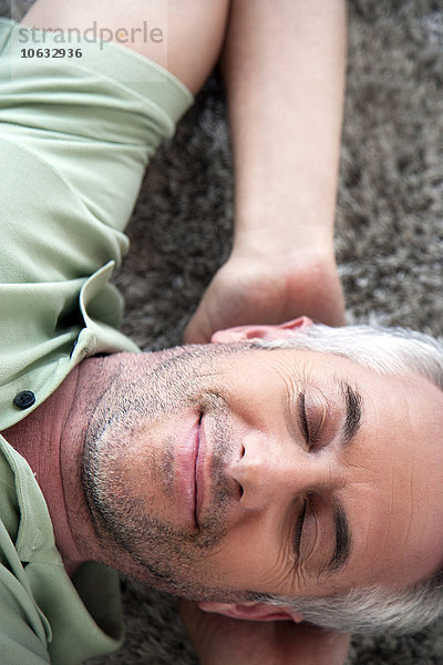Porträt eines lächelnden Mannes mit geschlossenen Augen  der sich zu Hause auf einem Teppich entspannt.