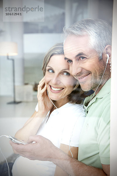 Portrait eines lächelnden Paares mit Kopfhörern und mp3-Player durchs Fenster schauend