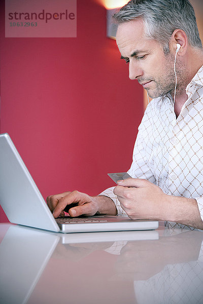 Porträt eines Mannes mit Kopfhörern  die bei der Benutzung eines Laptops eine Kreditkarte halten.