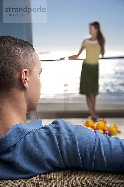 Junger Mann auf Couch mit Freundin auf dem Balkon am Meer stehend