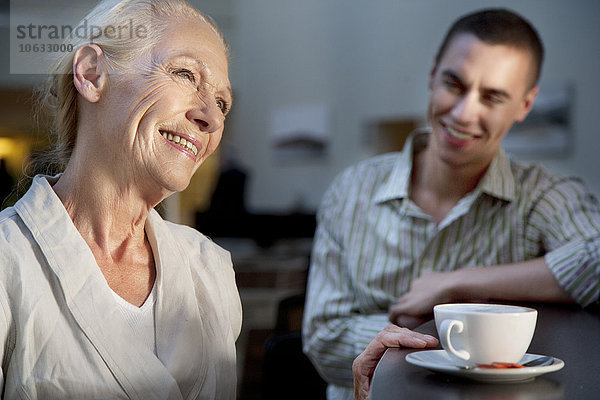 Lächelnde Seniorin mit Tasse Kaffee und jungem Mann im Hintergrund