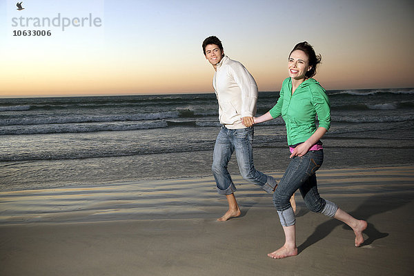 Junges Paar  das in der Abenddämmerung Hand in Hand am Strand läuft.