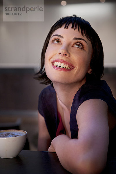 Lächelnde junge Frau mit einer Tasse Kaffee  die nach oben schaut.