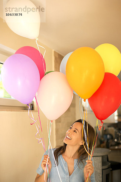 Fröhliche Frau steht und hält bunte Luftballons.