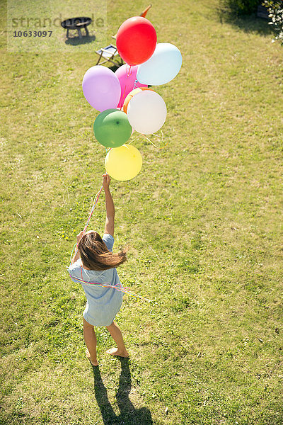 Frau steht im Garten und hält bunte Luftballons.