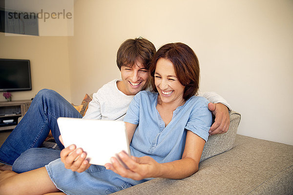 Glückliches Paar entspannt sich auf der Couch und schaut sich das digitale Tablett an.
