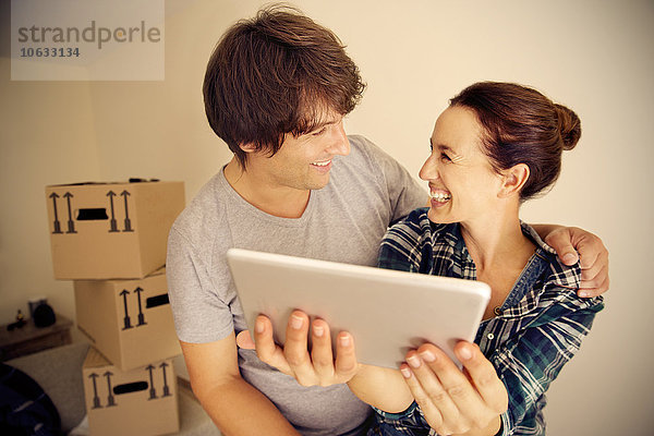 Glückliches Paar mit digitalem Tablett und Kartons im Hintergrund