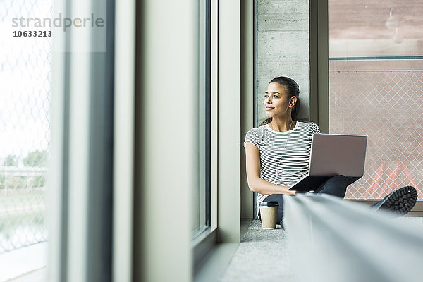 Junge Frau sitzt auf dem Boden im Büro mit Laptop