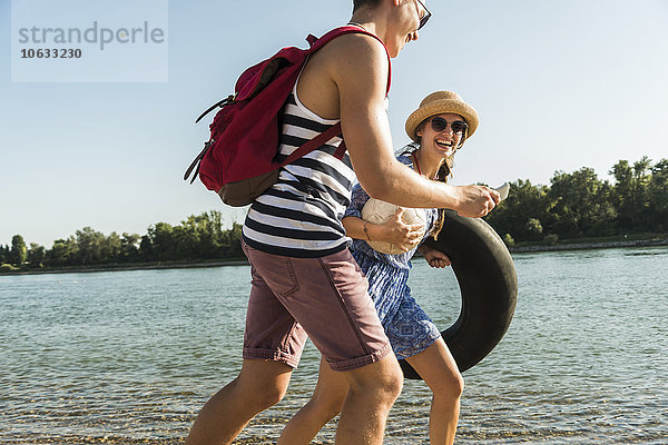 Junges Paar mit Schlauch und Handy beim Spaziergang am Flussufer