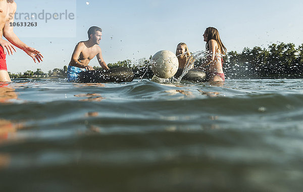 Glückliche Freunde mit Schläuchen und Ball im Wasser