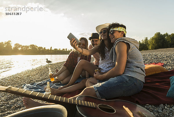 Freunde  die bei Sonnenuntergang einen Selfie am Flussufer nehmen.