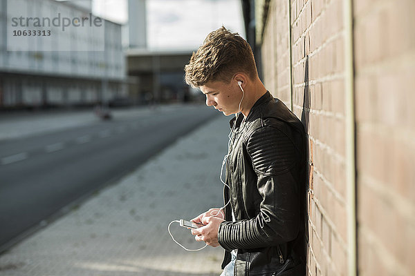 Junger Mann mit Ohrstöpseln beim Blick aufs Handy
