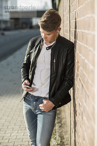 Junger Mann mit Ohrstöpseln beim Blick aufs Handy