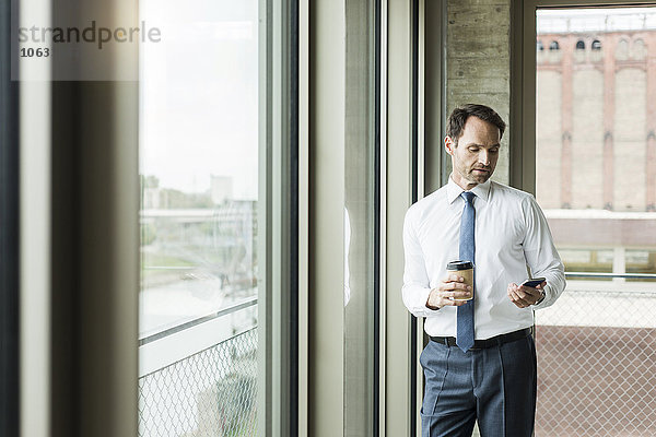 Porträt eines Geschäftsmannes mit Kaffee zum Anschauen seines Smartphones