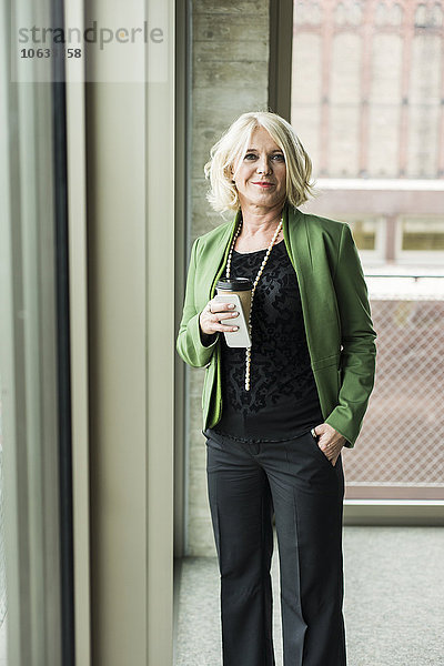 Portrait der blonden Geschäftsfrau mit Kaffee zum Mitnehmen und Smartphone