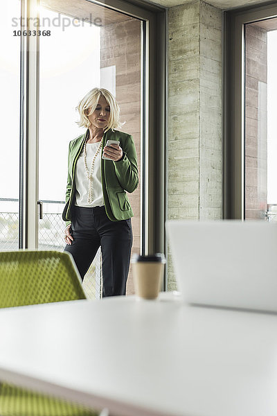Porträt einer blonden Geschäftsfrau mit Blick auf ihr Smartphone im Büro