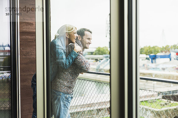 Ein glückliches Paar steht zusammen auf dem Balkon und schaut in die Ferne.