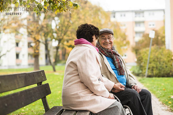 Älterer Mann im Rollstuhl hält Hände mit Frau auf der Bank