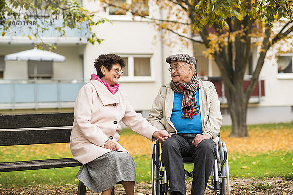 Seniorin auf der Bank neben dem Ehemann im Rollstuhl sitzend