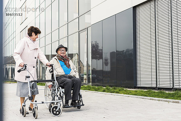 Seniorin mit Rollator und Senior im Rollstuhl auf dem Bürgersteig