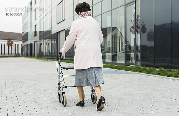 Ältere Frau  die mit einem Rollator auf dem Bürgersteig geht.