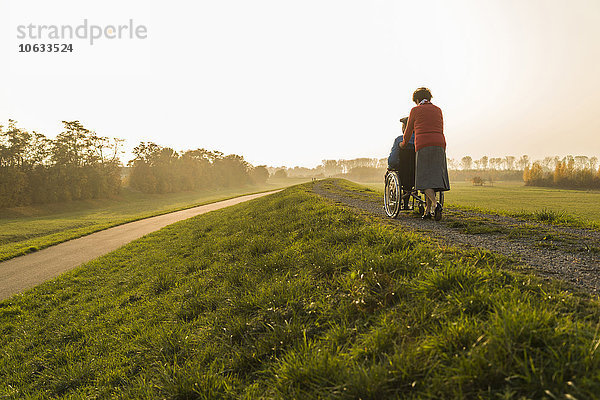 Seniorin schiebt Ehemann im Rollstuhl in der Natur