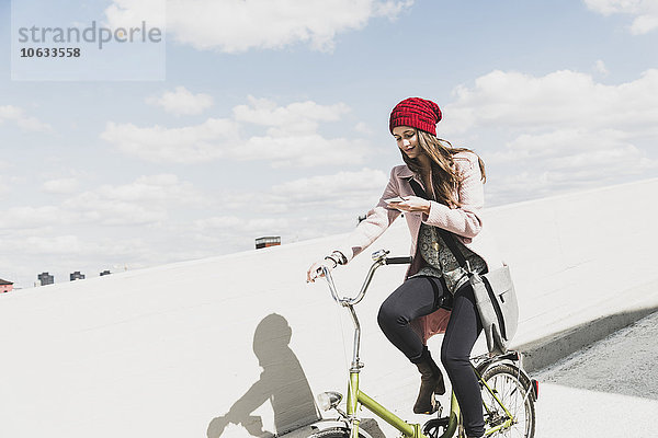 Junge Frau auf dem Fahrrad beim Blick aufs Handy