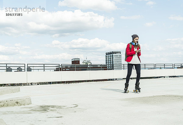 Junge Frau mit Handy und Inline-Skates auf Parkebene