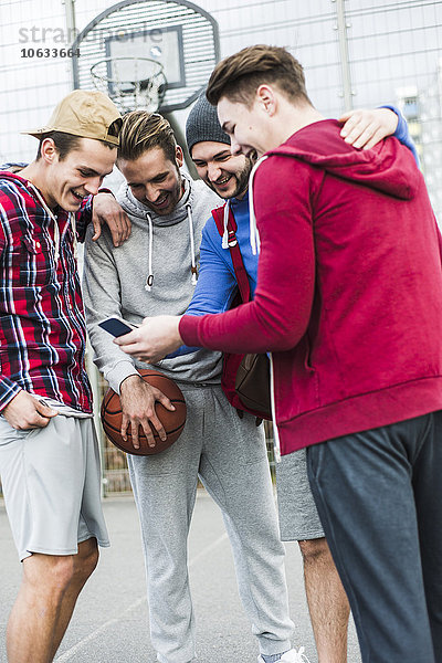 Junge Basketballspieler mit Smartphone lachend