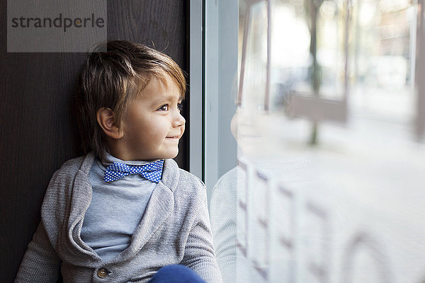 Porträt eines lächelnden kleinen Jungen mit Fliege  der durch das Schaufenster blickt