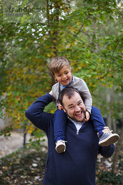 Ein lachender kleiner Junge  der auf den Schultern seines Vaters sitzt.