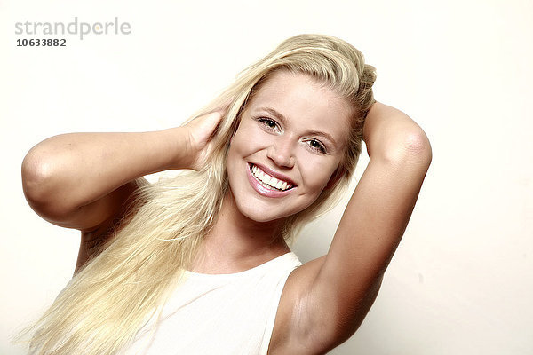 Porträt einer lächelnden blonden jungen Frau mit Händen im Haar