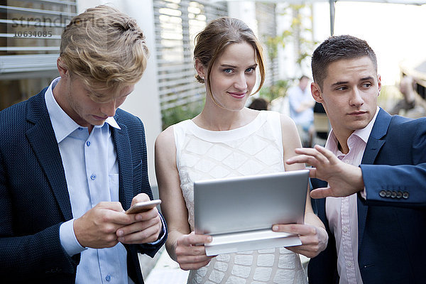Drei junge Geschäftsleute mit digitalem Tablett und Handy im Freien