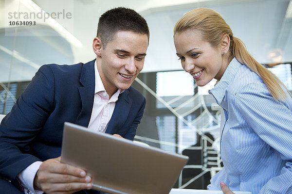 Lächelnder Geschäftsmann und Geschäftsfrau beim Betrachten des digitalen Tabletts im Büro
