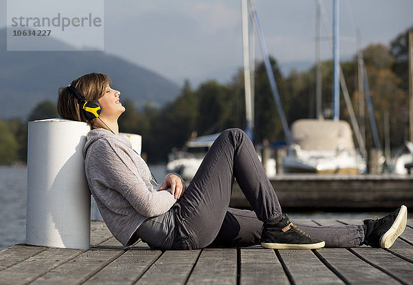Österreich  Mondsee  junge Frau auf einem Steg am Mondsee  Musik hören mit Kopfhörern