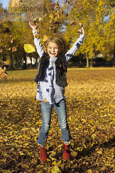 Fröhliches kleines Mädchen wirft Herbstlaub beim Sprung in die Luft