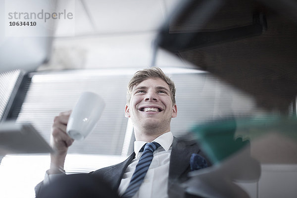 Lächelnder Geschäftsmann mit Kaffeetasse im Büro