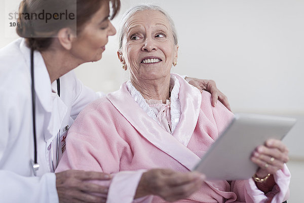 Arzt und lächelnder älterer Patient im Rollstuhl mit digitalem Tablett